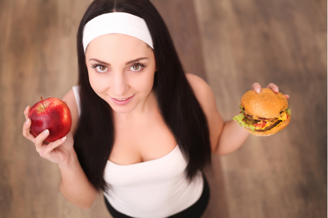 Молодая девушка держит в руках яблоко и чизбургер.